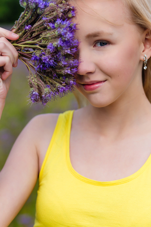 Closeup portrait of a Beautiful young girl in a yellow dress in a blooming summer field. Girl in purple flowers outdoors in summerの写真素材