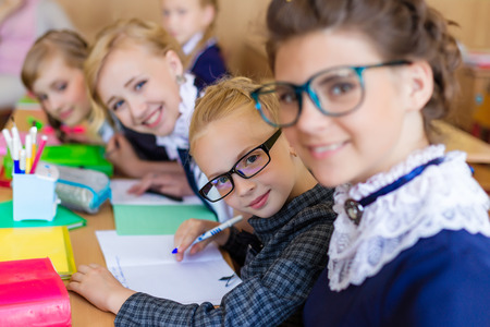 Girls at school desks. Girlfriends are sitting at school with books, notebooks and telephones. Children study in the school roomの写真素材