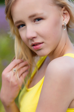 Closeup portrait of a Beautiful young girl in a yellow dress in a blooming summer field. Girl in purple flowers outdoors in summerの写真素材