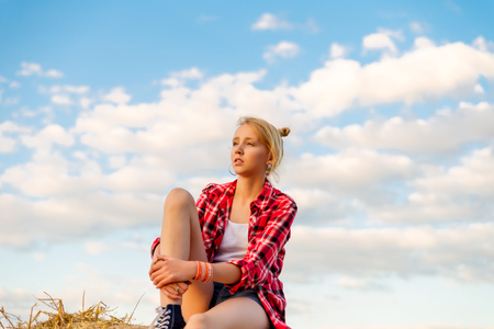 Young girl on straw sheaves in a field. Girl on a wheat field in the rays of the setting sun.の写真素材