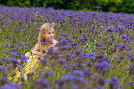 Beautiful young girl in a yellow dress in a blooming summer field of purple flowers outdoors in summerの写真素材