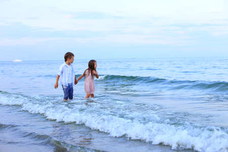 Two children run along the sea near the shoreの写真素材