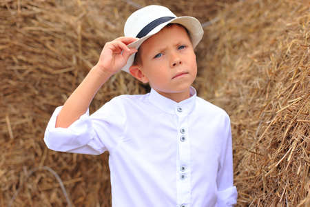 A cute boy is high under the sky on a haystack in the hay season.の写真素材