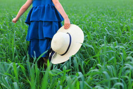 A little girl with a hat in her hands runs on a green field in summerの写真素材