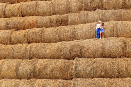 Two children are high under the sky on a haystack in the hay season. In the summer in the village on...