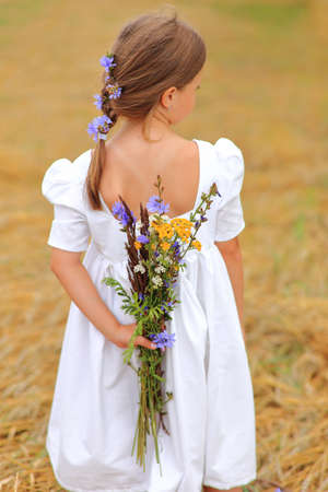 Little girl with a bouquet of wildflowers in her hands in a wheat field.の写真素材