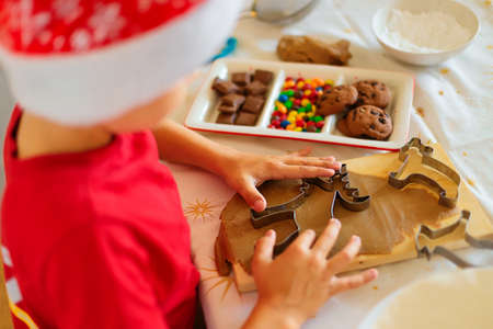 A boy in a santa hat prepares cookies in the kitchen.