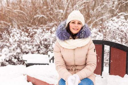A young girl sits on a bench in a snowy parkの写真素材