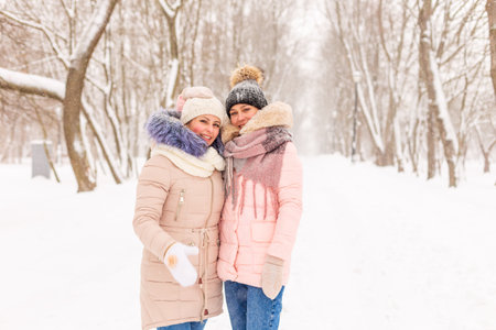 Two girls are walking in a winter park in the snow.