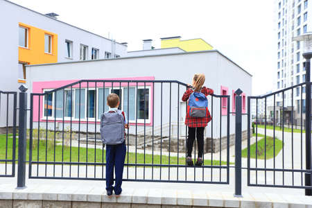 Children with briefcases over their shoulders on the background of the school.の写真素材