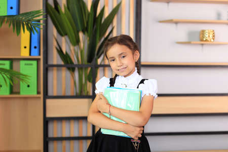 Portrait of a girl in a school uniform with notebooks in her hands. Young schoolgirl in the class....
