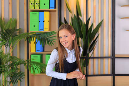 A child in a school uniform is posing in the classroom. A young schoolgirl looks at the camera. Girl in a lesson at schoolの写真素材