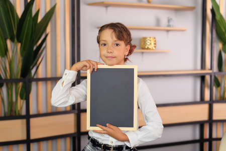A young girl holds in her hand a drawing board in a frame. The child holds the frame in his hands. A schoolgirl holds a blackboard with chalk.の写真素材