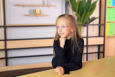 A child in a school uniform is posing in the classroom. A young schoolgirl looks at the camera. Girl in a lesson at schoolの写真素材