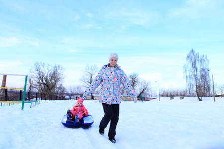 Mom and daughter ride a tubing in winter. The family spends time outside in winter. Sled games