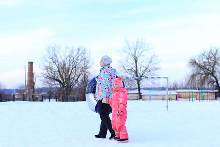 Mom and daughter ride a tubing in winter. The family spends time outside in winter. Sled gamesの写真素材