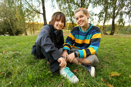 Two young women are relaxing in a beautiful natural setting during summer. They are laughing and enjoying each other's company. The scene radiates joy and friendship, capturing a perfect moment of carefree summer days spent outdoors.の写真素材