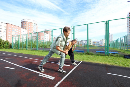 Two children stand alongside their coach on a running track near a school, preparing for an upcoming...