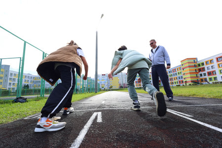 Two children stand alongside their coach on a running track near a school, preparing for an upcoming race. The coach provides encouragement, fostering a spirit of teamwork and motivation in this vibrant outdoor setting. Childrens running competitionの写真素材