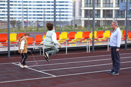 Two children joyfully jump rope with their physical education teacher on a specially designed outdoor sports playground. The vibrant setting encourages teamworkの写真素材