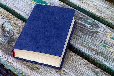 A blue book lies on shabby old boards on a street bench