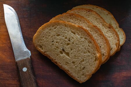 Sliced slices of golden bread on a wooden cutting board. Sliced sliced bread on a dark board and...