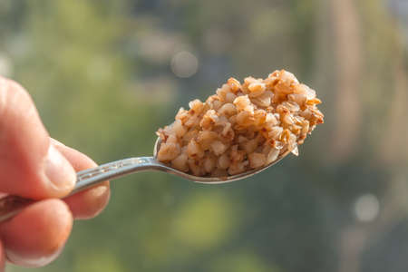 Buckwheat porridge in a metal spoon in the defocused background
