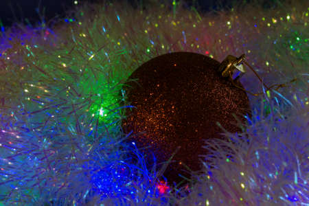 New Year's Eve background from a Christmas tree toy lying on tinsel illuminated from below with a multi-colored gerland. Christmas background in low cryptic keyの写真素材