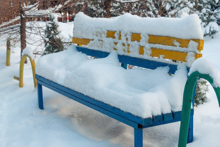A yellow-blue bench covered with a thick layer of snow in the parkの写真素材