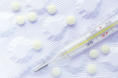 medical background thermometer on top of packaging with pills in bright light toning