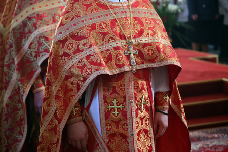 Orthodox priest with a crucifix in red clothes
