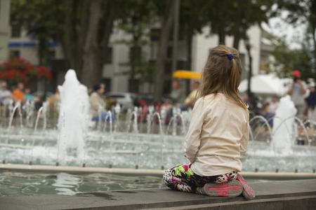 Young girl  sitting near fountain and looking on the water