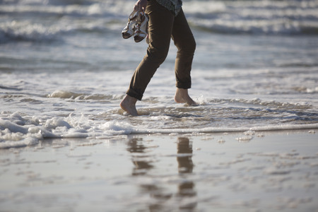 woman's legs walking by sea shore. Close up of sea shore with woman walking through waves.