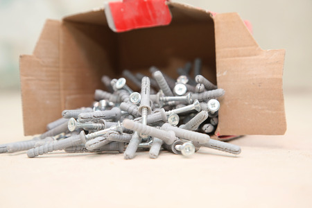 carton box ful of screws with wall plugs on the floor