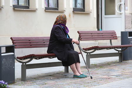 Woman with her walking stick in the street sitting on the benchの写真素材