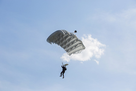Parachutist with white parachute is flying in the blue sky