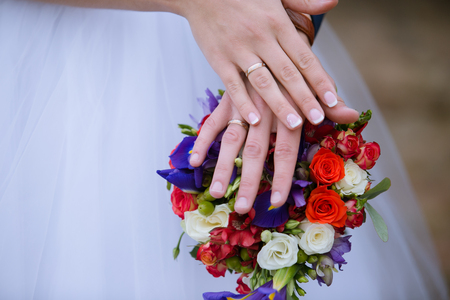 Wedding bouquet - groom and bride's hands with elegant manicure and gold ringsの写真素材