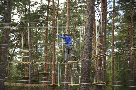 Man climbing in adventure rope park in safety equipment between treesの写真素材