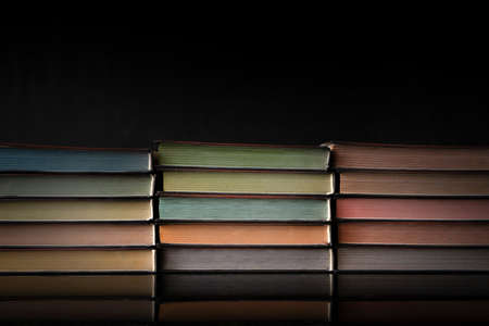 Old books with colored pages lie in stacks on a table on a very dark background. Vintage style.の写真素材