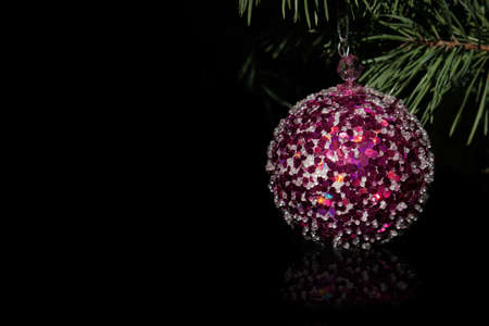 Christmas decoration ball on a pine branch. Isolated over black background. Focus on the foreground.の写真素材