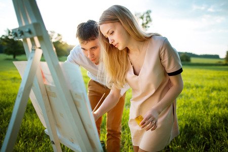 Young couple painting on an easel in a fieldの写真素材