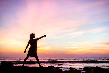 Silhouette of a girl standing on a rock at sunsetの写真素材