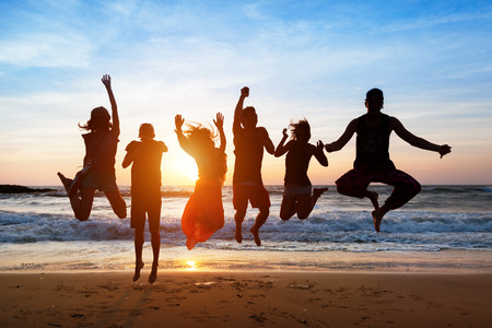 Six people with a shadow cast on them are jumping on beach at sunset.