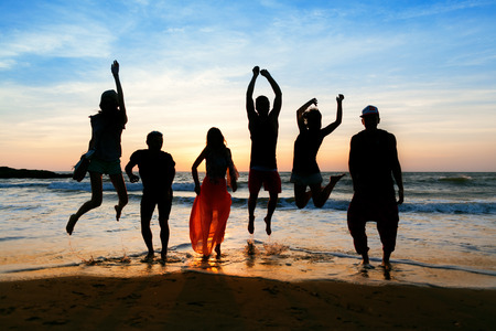 Six people with a shadow cast on them are jumping on beach at sunset.の写真素材
