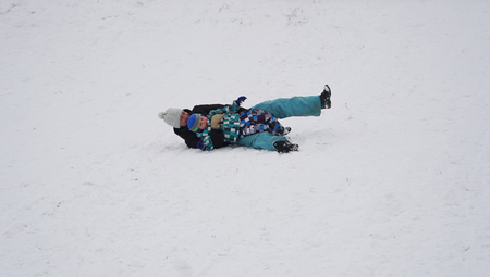 Smiling mother falls with her baby on the snow in winter park.の写真素材