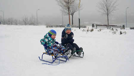 Two little children sledding on the snow-covered road in winterの写真素材