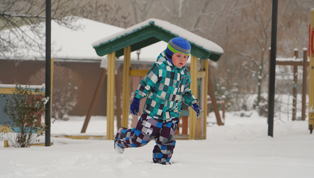 Little child run on the snow-covered lawn in winter park in the children's townの写真素材