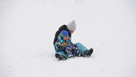 Mother sitting with her baby on the snow in winter park foolingg around .の写真素材