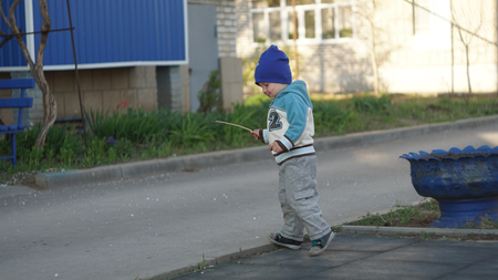Cute Young Boy Walking with Stick on the sidewalkの写真素材