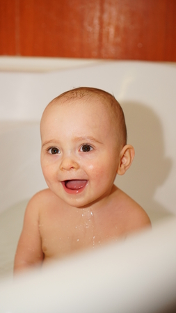 Funny little child smiling and playing with water in a bathroom. Toddlers bathes.の写真素材